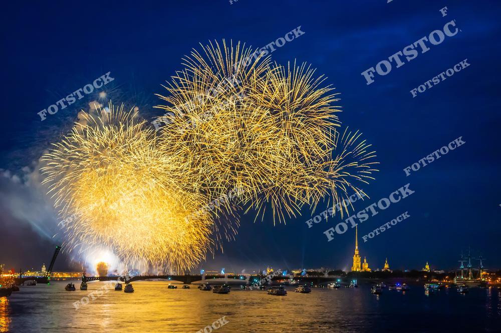 На фотографии изображен красочный фейерверк, вспыхнувший над Невой в Санкт-Петербурге. На заднем плане можно увидеть Петропавловскую крепость с её золотым шпилем, который придает сцене историческую значимость. Вечерние огни и отражение салюта в водах Невы создают атмосферу торжества и праздника. Этот вид особенно популярен в дни городских праздников, когда Санкт-Петербург сияет от праздничных огней.